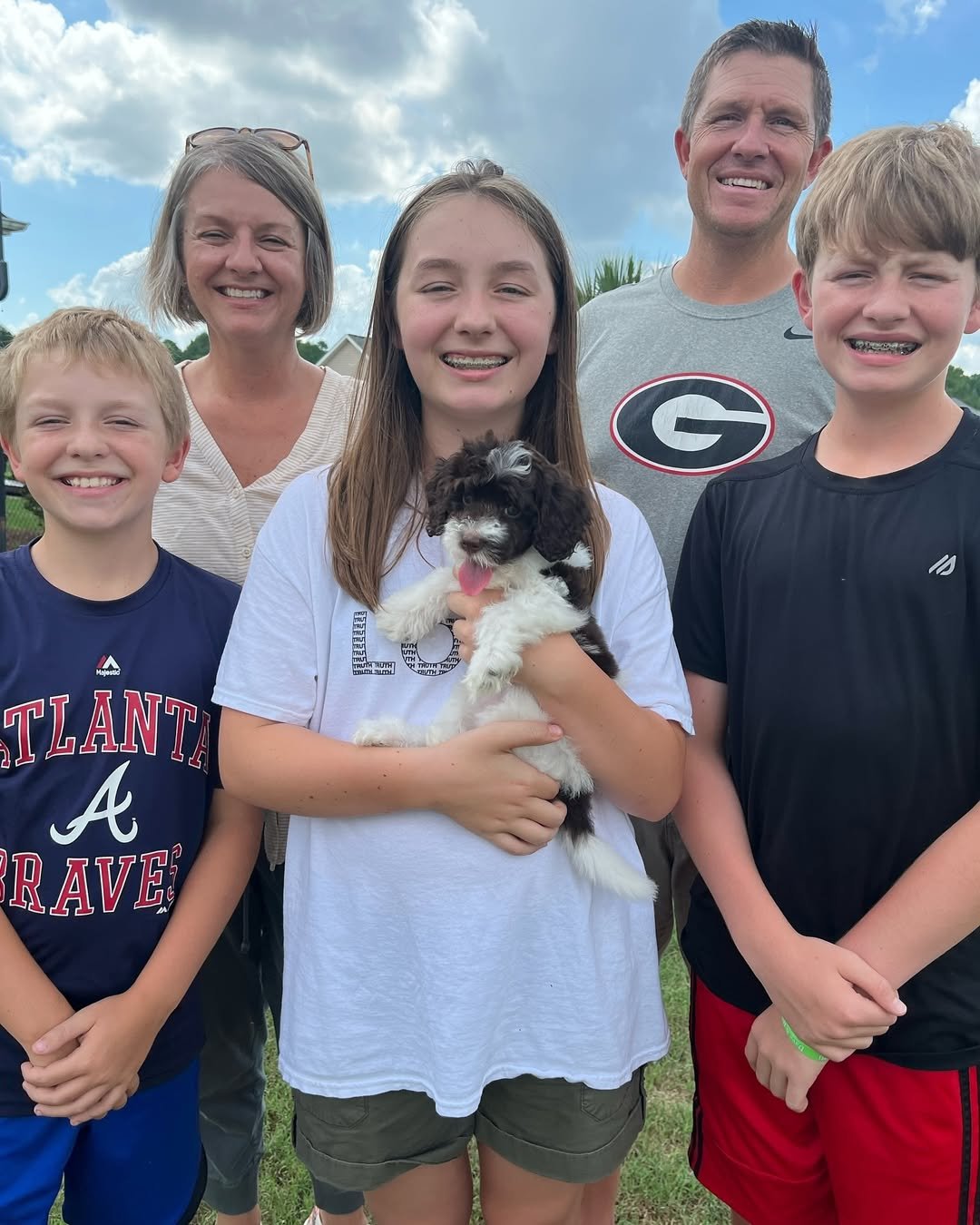 Smiling family outdoors with a girl holding a small black and white puppy on a grassy lawn